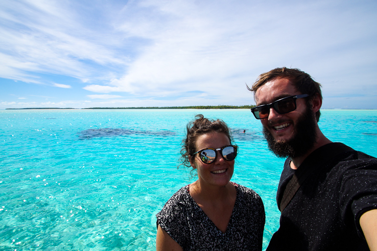 Die beiden Blogger Anne und Clemens lächeln von einem Vaka auf dem hellblauen Meer der Cook Insel Aitutaki strahlend in die Kamera.