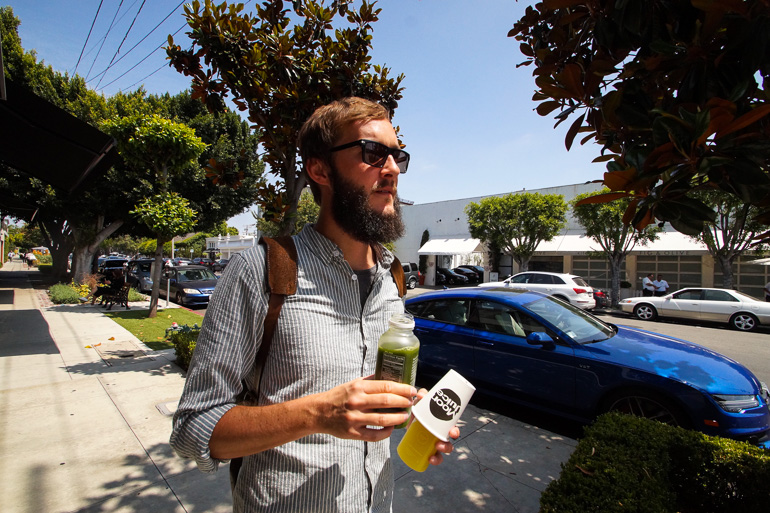 Ein Mann läuft durch die Straßen von Los Angeles und hält in beiden Händen gesunde und vitaminreiche Säfte.