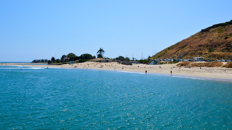 Das blaue Wasser glitzert in der Sonne am Santa Monica Malibu Strand, am feinen Sandstrand tummeln sich Badegäste.