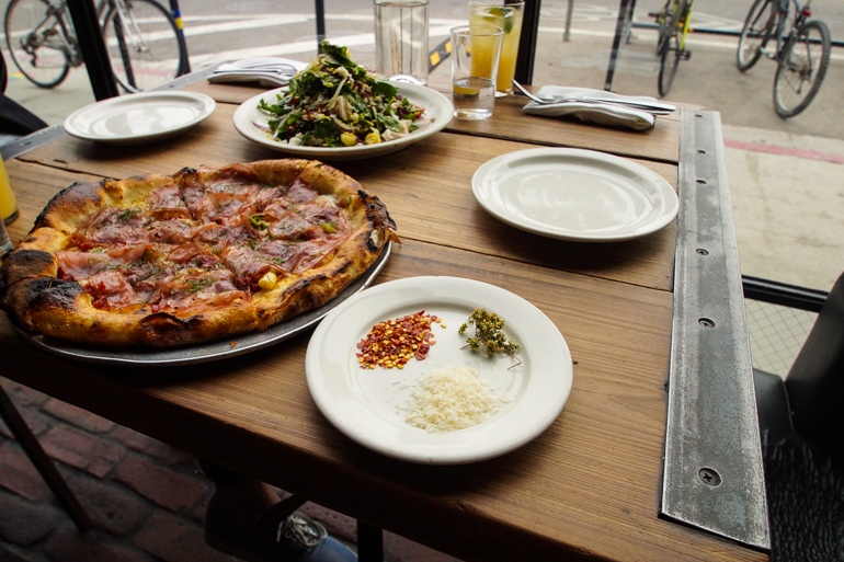 In Santa Monica am Venice Beach serviert das Restaurant Gjelina eine Steinofenpizza, am Tisch wurde noch ein Teller mit Gewürzen und ein Salat gereicht.
