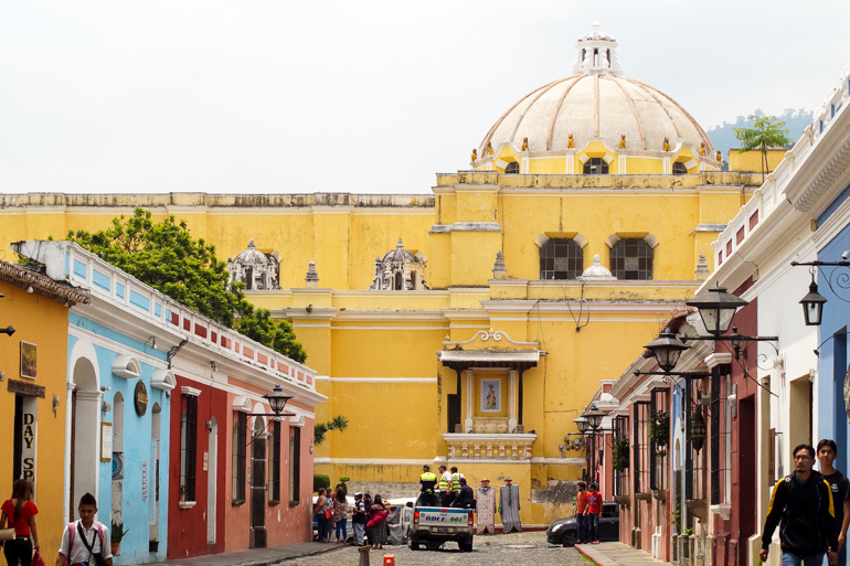 Eine Martkstraße in Antigua mit bunten Häuserfassaden führt zu einer in gelb getünchten Kathedrale.