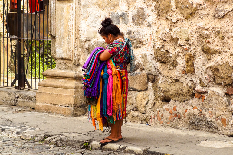 Eine Maya-Frau hält auf einer Straße von Antigua bunte Stoffe in der Hand.