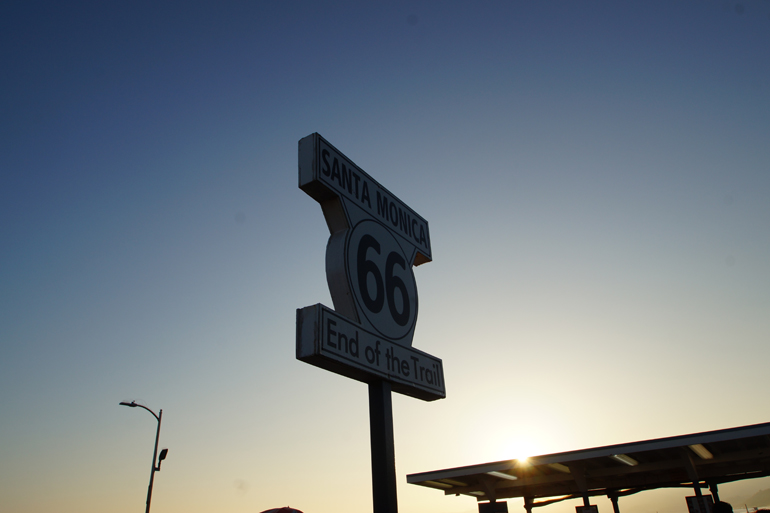 Ein Straßenschild beschriftet mit der Zahl 66 bei Sonnenuntergang in Santa Monica.