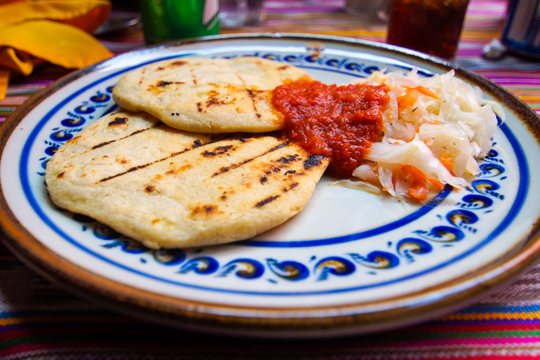 In einem Restaurant in Guatemala werden Pupusas, Tortillas mit roter Soße und Gemüse auf einem blau-weißen Teller serviert.