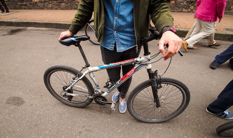 On the streets of Colombia's Bogotá, a man holds his bicycle while the camera focuses on his bike.