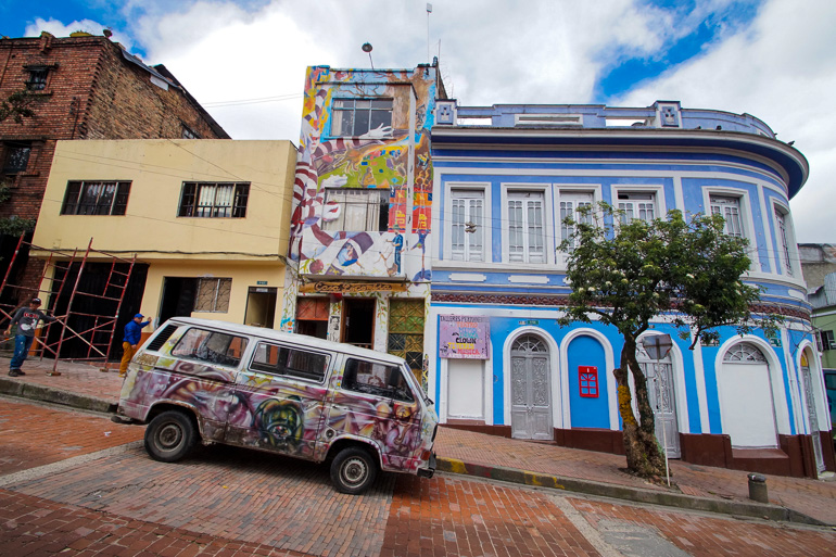 A colorfully spray-painted VW bus is parked in the streets of Colombia's capital, Bogotá.  In the background you can see graffiti on the house facade.