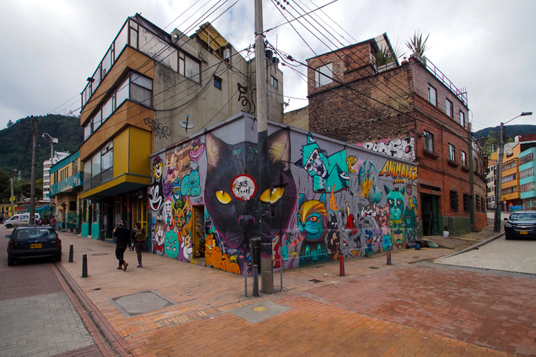 An einer Häuserecke in Bogotá in Kolumbien wurde eine Straßenlaterne in die Graffitikunst, das ein schwarzes Katzengesicht zeigt, integriert.