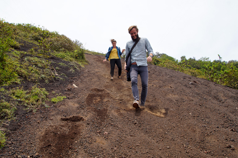 Ein Pärchen steigt fröhlich den brau-grauen sandigen Weg vom Vulkan-Pacaya ab.