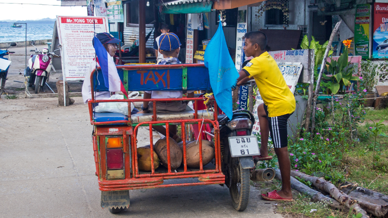 Einheimische Kinder unterhalten sich nach ihrem Einkauf an einem Motorradtaxi auf Koh Mook, Thailand.