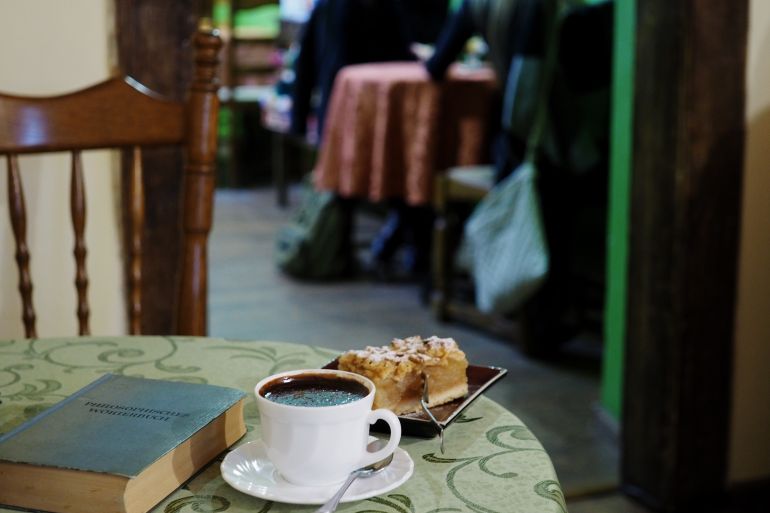 Auf einem Tisch im Schokoladencafe von Lublin wurde auf der grünen mit Ornamenten verzierten Tischdecke eine Tasse mit dunkler Schokolade und ein Stück Apfelkuchen angerichtet.