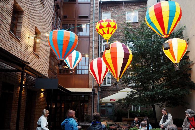 In einem Innenhof eines Backsteingebäudes in Lublin wurde eine Lichterkette aus kleinen bunten Heißluftballons gespannt, darunter haben sich Gäste zum Geschmacksfestival eingefunden.