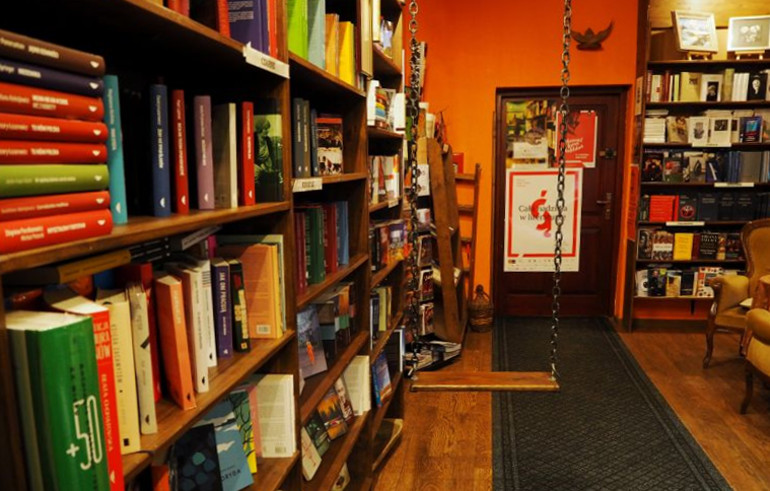 Im orange gehaltene Schokoladencafe in Lublin hängt eine Schaukel, umgeben von gefüllten Bücherregalen.