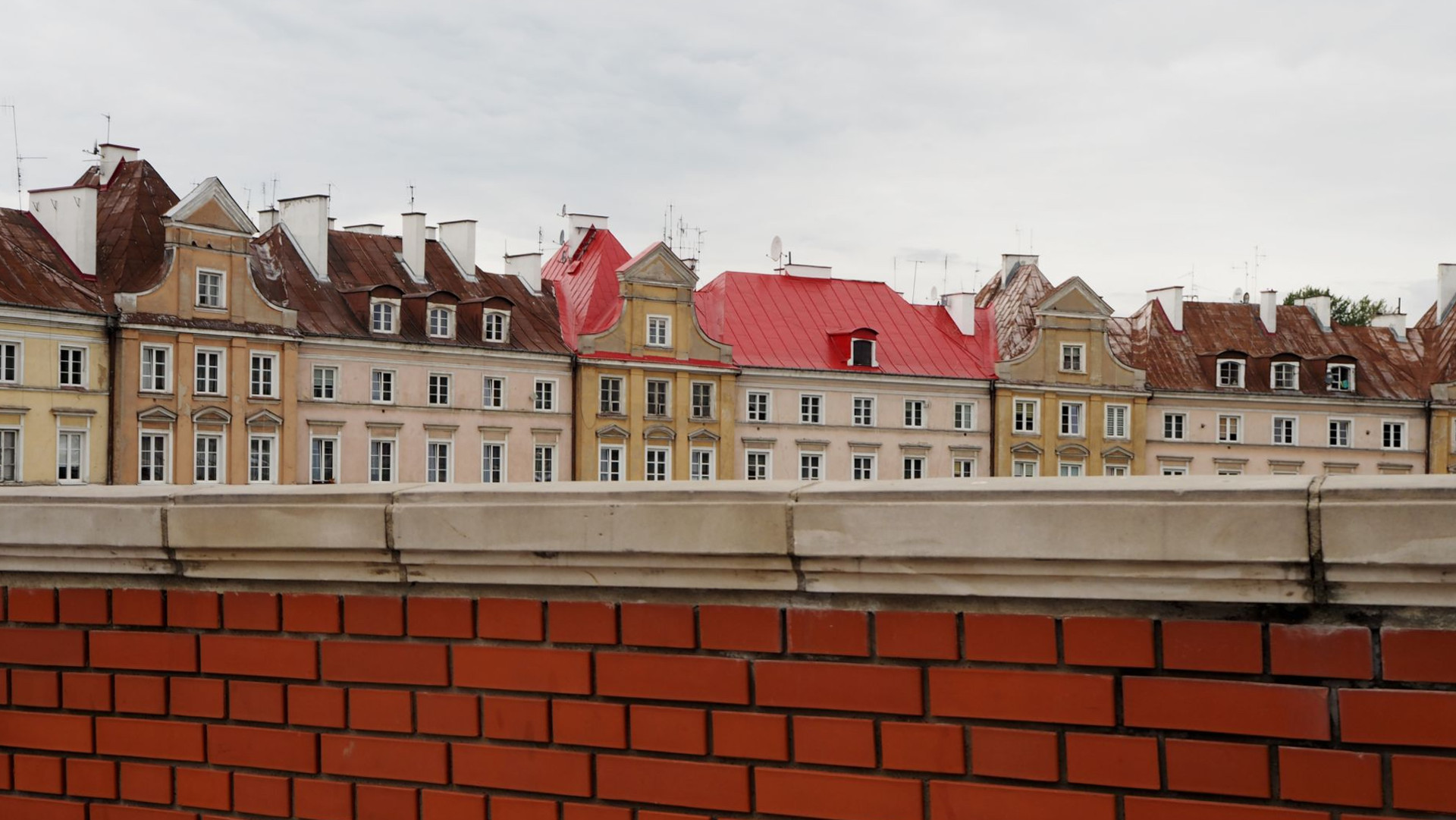 Hinter einer Steinmauer verbirgt sich ein in pastellfarbener Häuserzug der Altstadt Lublin in Polen.