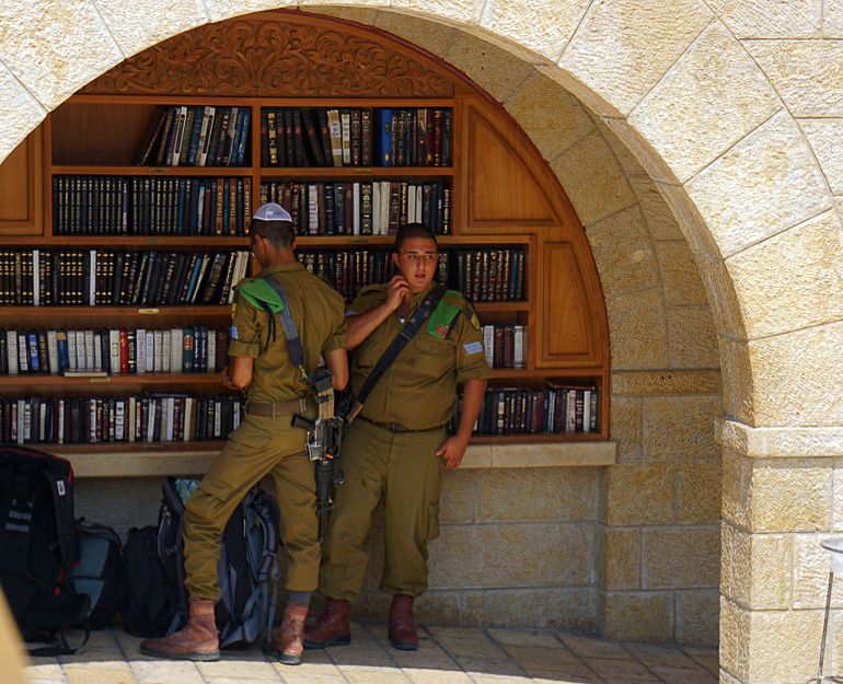 Zwei bewaffnete israelische Soldaten stehen in grüner Uniform unter einem Torbogen an einem Bücherregal in Jerusalem.