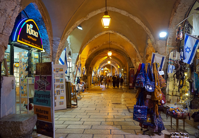 Unter beleuchteten Arkadenbögen in Jerusalems Altstadt bieten Händler in kleinen Shops ihre Ware an.