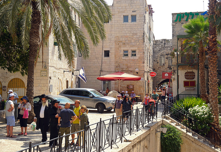In Jerusalems Jüdischen Viertel laufen Passanten entlang sandsteinfarbener Häuserfassaden und Palmen den Weg entlang.