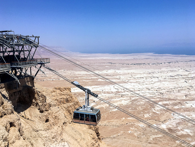 Eine Gondel der Seilbahn fährt entlang des Berges von Masada inmitten der kargen Wüstenlandschaft Israels empor.