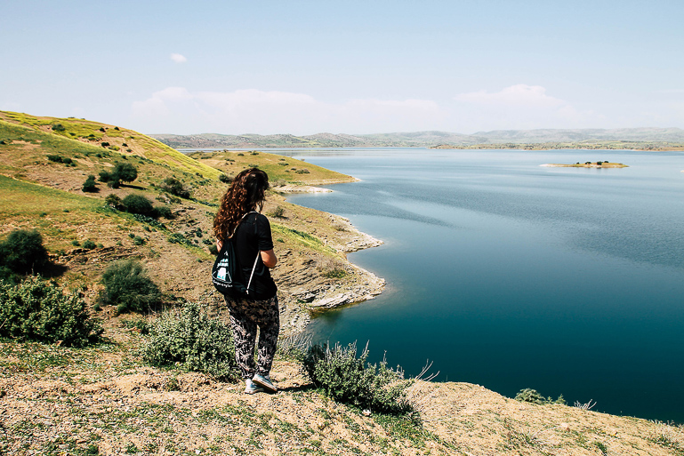 Eine Touristin steht in Marokko auf einem kleinen Hügel, ihr Blick ist auf den Stausee El Hansali gerichtet.
