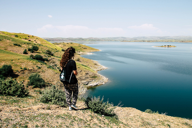 A tourist stands on a small hill in Morocco, her gaze is directed towards the El Hansali reservoir.