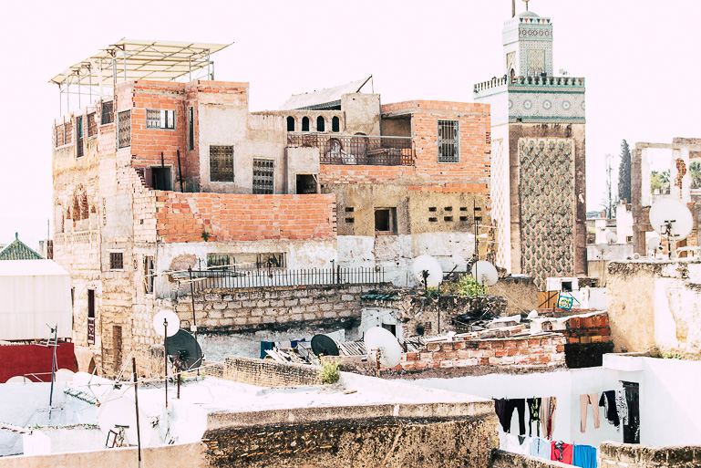 Auf den Dächern von Fez in Marokko liegt der Blick auf rote Ziegelsteinbauten, Wäscheleinen, Satellitenschüsseln und einer Moschee.