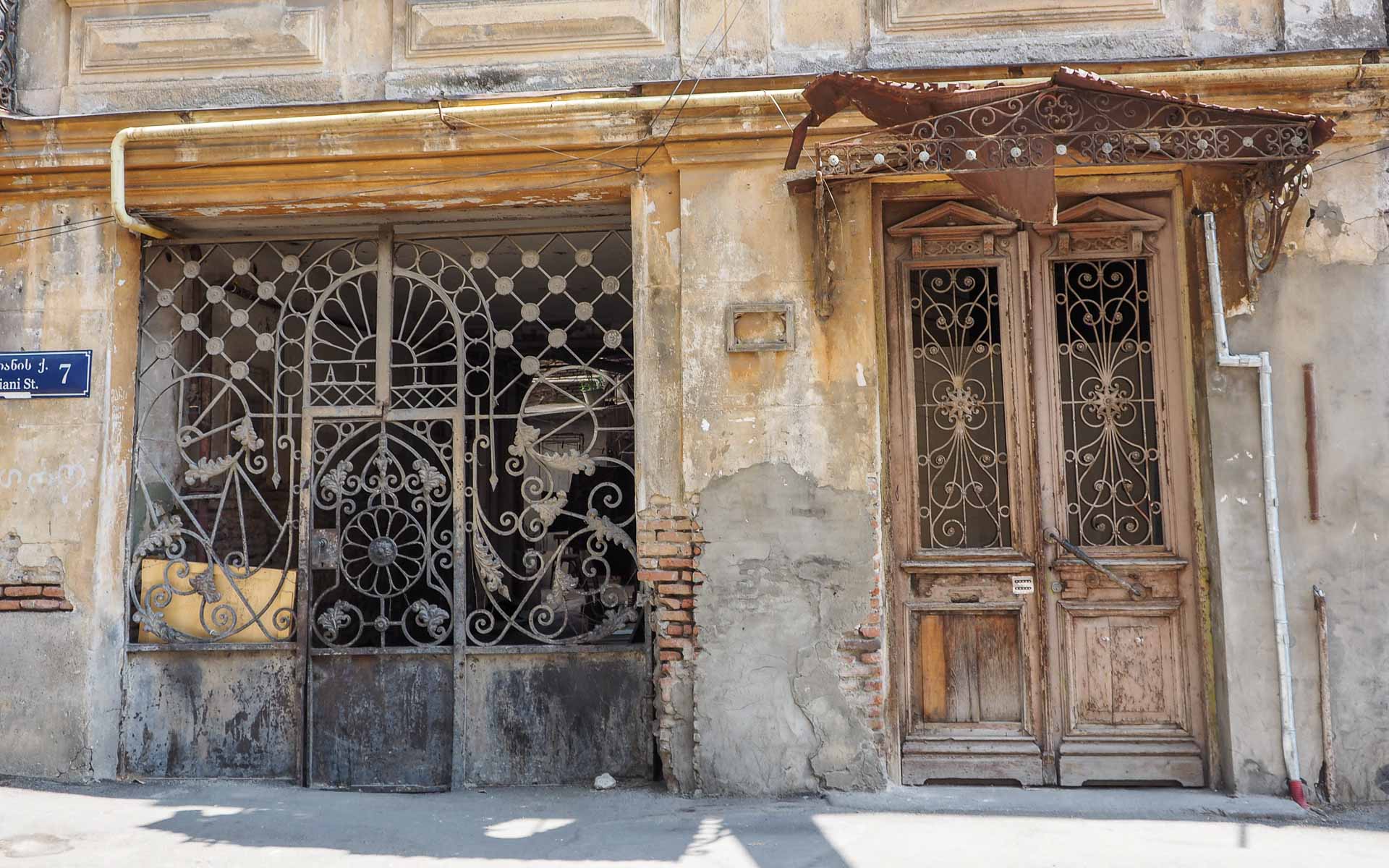 Eine bröckelnde Hausfassade mit altem verziertem Eisentor und Holztür ziert eine Straße von Tiflis Wohngegend Sololaki in Georgien.