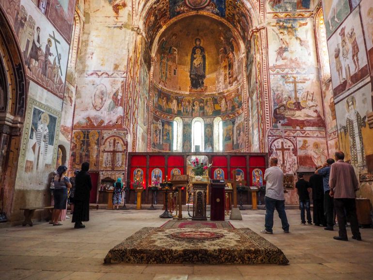 Besucher im Inneren der georgischen Klosteranlage Gelati beten Richtung Altar und der aufwendigen Malereien an den kuppelförmigen Wänden.