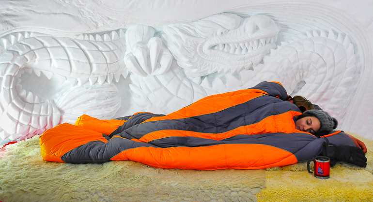 In einem Igludorf mit verzierten Schneewänden haben sich 2 Personen in warmen Schlafsäcken zum Schlafen gelegt.