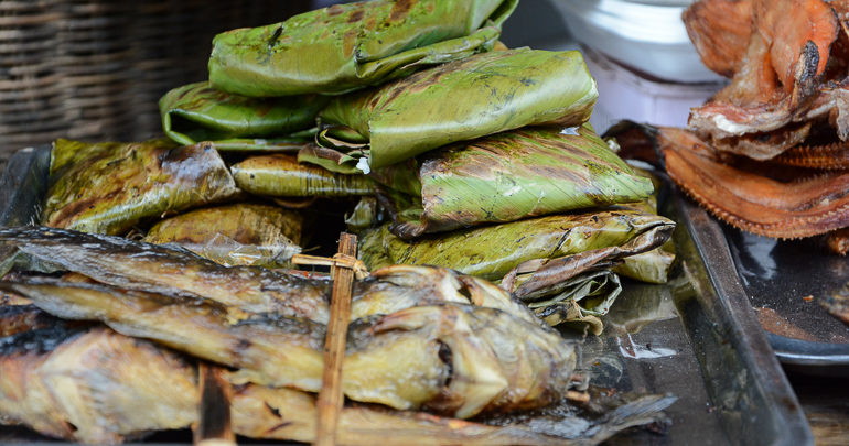 Fisch und gefüllte Blättertaschen werden an einem Streetfood-Stand im Phsar Nath Markt in Battambang auf der Kambodscha Rundreise zum Verzehr angeboten.
