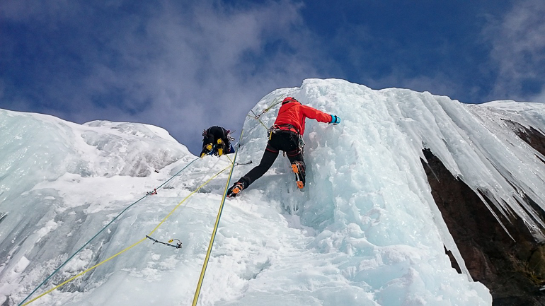An einem vereisten Berg üben sich zwei Sportler im Eisklettern.