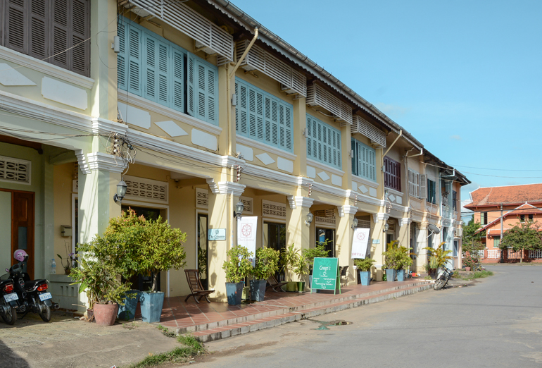 An den Arkaden der Häuser von Kampot stehen Sonnenschirme und Pflanzen davor.