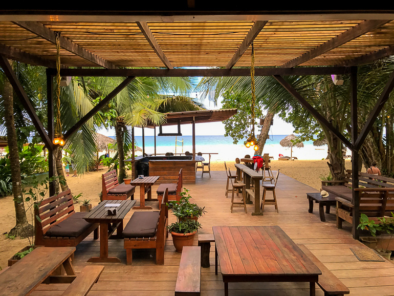 At the accommodation Palmar on the island of Bastimentos there is a wooden terrace with chairs between palm trees and a view of the beach.