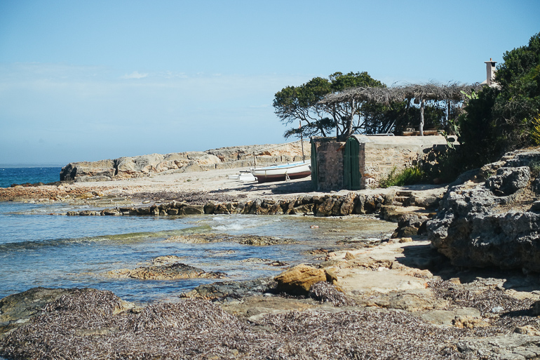 Auf Mallorca wurde am Meeresufer ein altes Fischerhaus in die Felsen gebaut, daneben liegt ein kleines Boot.