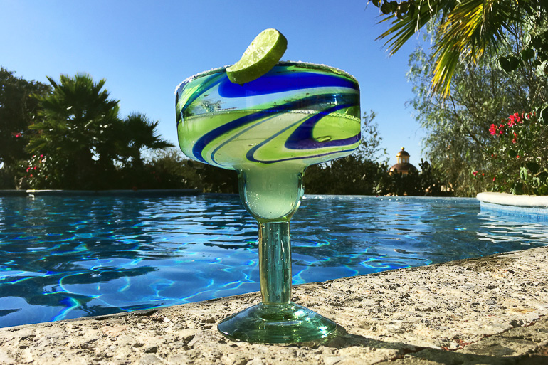 Ein Margarita-Cocktailglas mit einer Limettenscheibe steht am Randes Pools der Rancho las Cascadas.