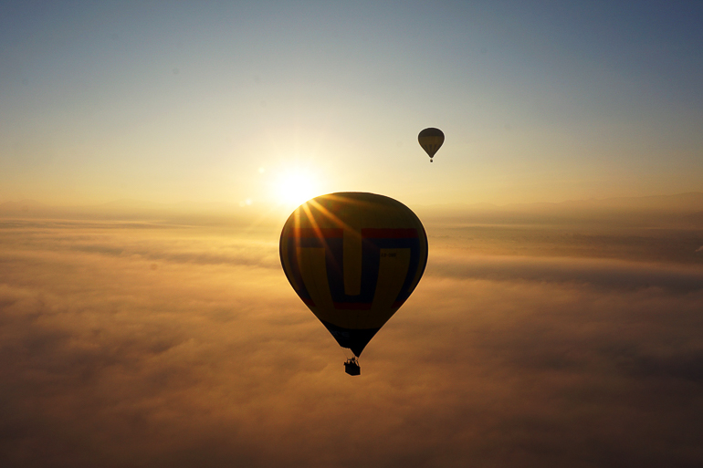 Ein Heißluftballon fliegt über den Wolken von Mexiko, genauer gesagt über den Pyramiden von Teotihuacán in die Abendsonne.