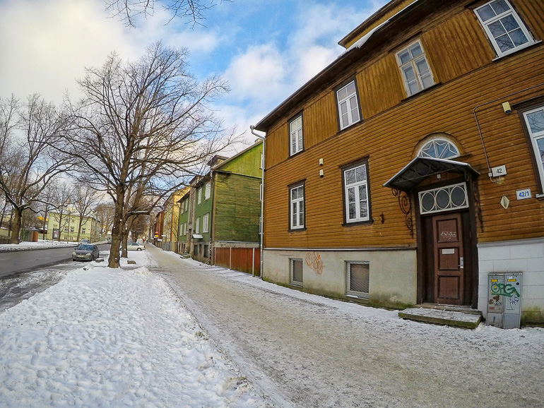 Der Blick auf die Straßen von Tallinns Viertel Kalamaja zeigt bunte Holzhäuser auf dessen Gehweg Schnee liegt.