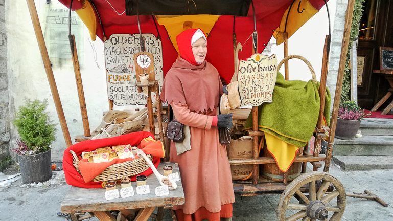 Eine Frau in mittelalterlicher Kleidung verkauft an ihrem Bollerwagen-Marktstand in Tallinn Makronen- und Mandelprodukte.