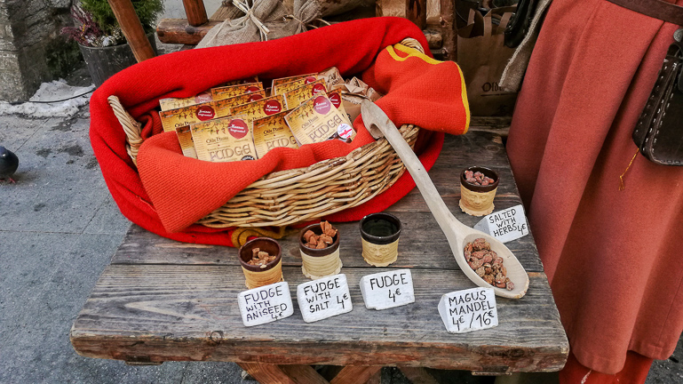 Auf einem mittelalterlich wirkendem Markt in Tallinn werden auf einem alten Holztisch Karamellbonbons angerichtet in einem Körbchen zum Verkauf angeboten.