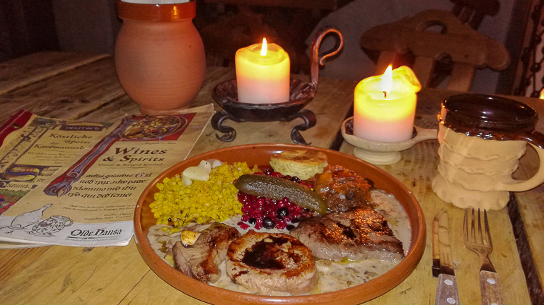 In Tallinns Restaurant Olde Hansa wird ein Gericht mit Wildfilet auf einen Tonteller bei Kerzenlicht und Tonkrug serviert.