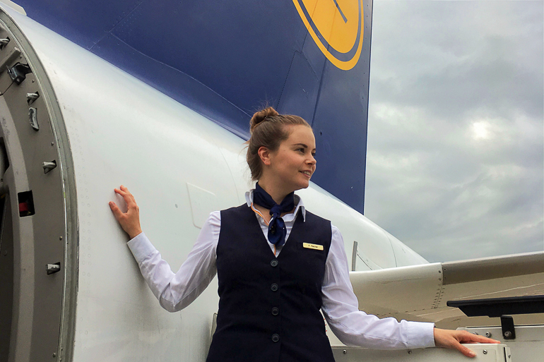 Eine Stewardess steht an der geöffneten Tür eines Flugzeuges und erwartet die Passagiere.