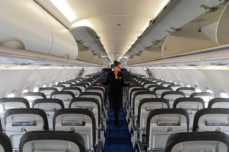 Im Innenraum eines Flugzeugs geht eine Flugbegleiterin den Flur entlang und überprüft die Sitzreihen.