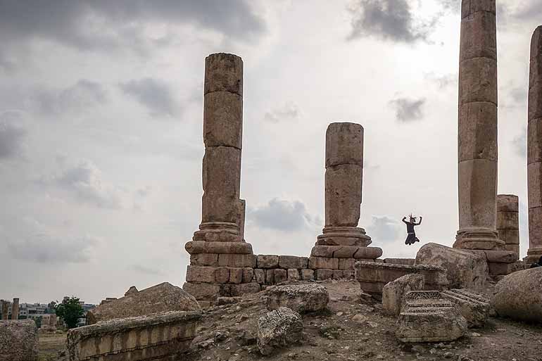 Eine Frau springt vor Freude zwischen Säulen in Ammans Zitadelle.