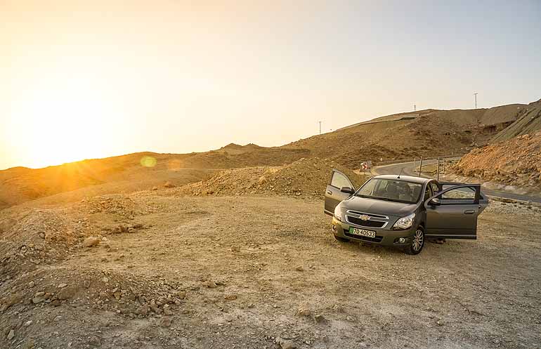 Ein Mietwagen steht mit geöffneten Türen bei Sonnenaufgang auf einer Schotterstraße Jordaniens.