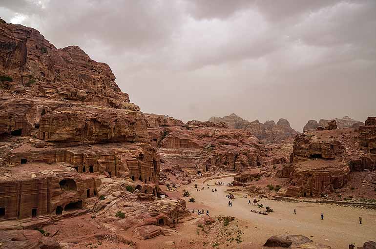 Felsformationen lassen in Petra, Jordanien die einstigen Unterkünfte der Einwohner erkennen, auf dem Weg zwischen den Felsformationen sind Menschen und Kamele unterwegs.