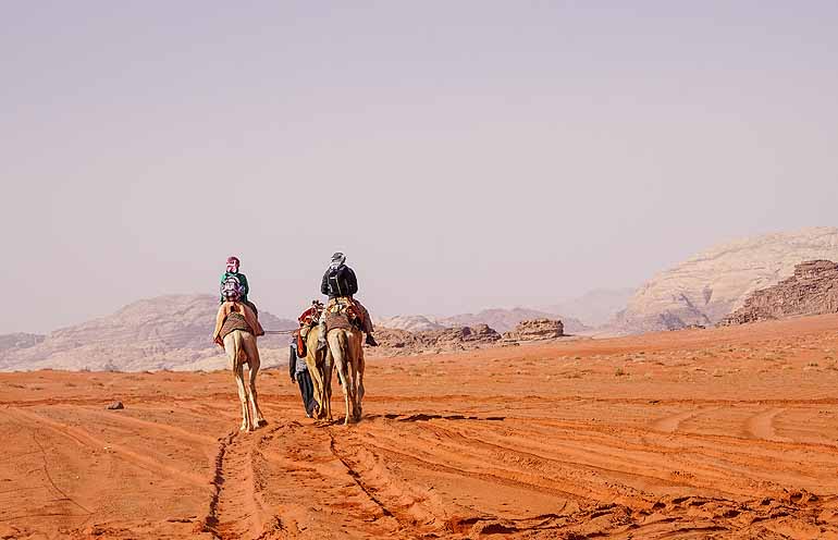 In Wadir Rum, Jordanien reitet eine Gruppe auf Kamelen durch die Wüste - Jordanien ist ein echtes Trendreiseziel.