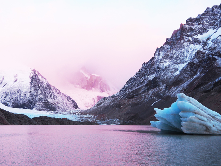 Sunrise at Laguna Torre in Patagonia bathes the lake and mountains in a purple light.