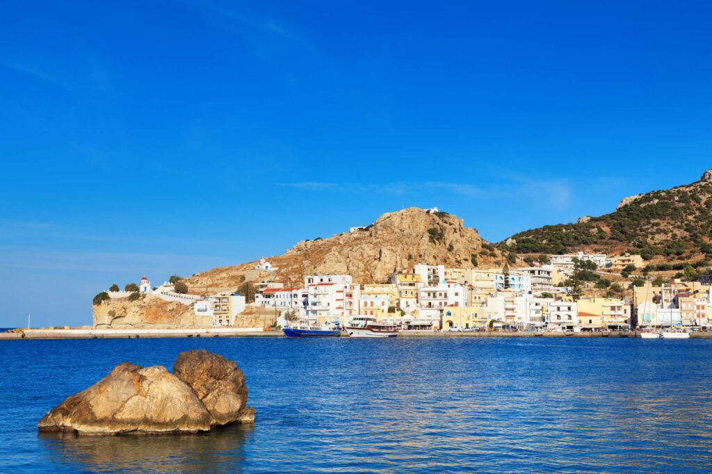 Vom Strand Pigadia aus genießt man den Blick über das Meer auf die am Felsen liegende Stadt Pigadia auf Karpathos.