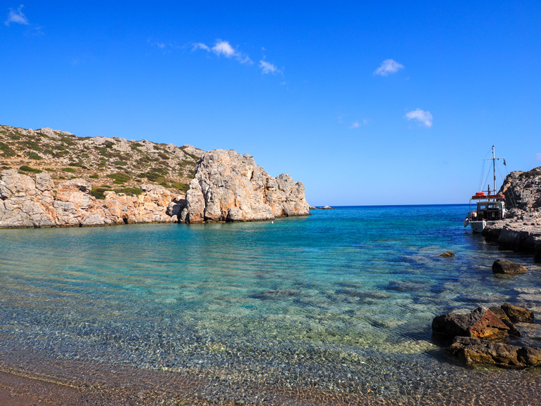 Angelehnt an einer Felsformation in der abgeschiedene Alimoúnta-Bucht in Karpathos hat ein kleines Segelschiff Rast eingelegt.