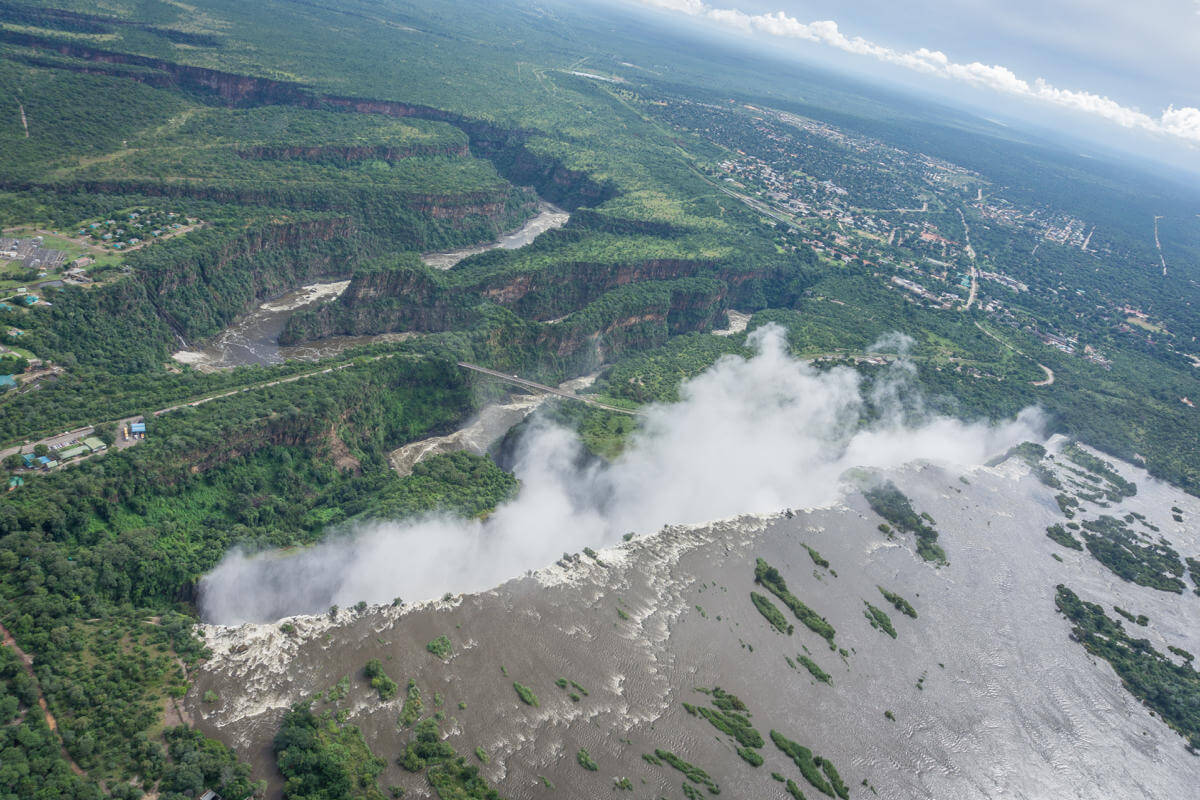 View of the vast area of ​​Victoria Falls and its spray rising into the sky from a helicopter.