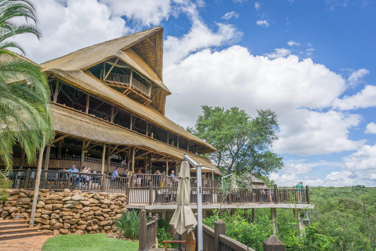 Inmitten grüner Natur steht die Victoria Falls Safari Lodge mit ihrem spitzen Reetdach und ihrer riesigen Holzterrasse.