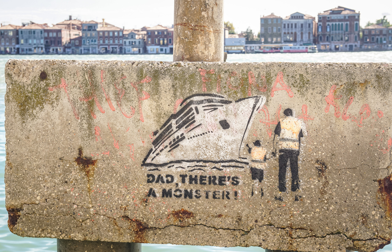 Ein Graffiti am Hafen weist auf die Probleme Venedigs durch sogenannten Overtourism - insbesondere durch Kreuzfahrttouristen - hin.
